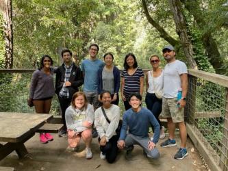 A group of people pose for a photo outside by a picnic table.