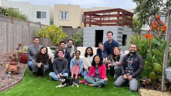 A smiling group of people sitting in on the grass in a backyard.