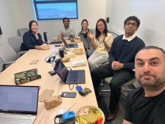 The Doris Wang lab sits around a conference table with their lunches and laptops.